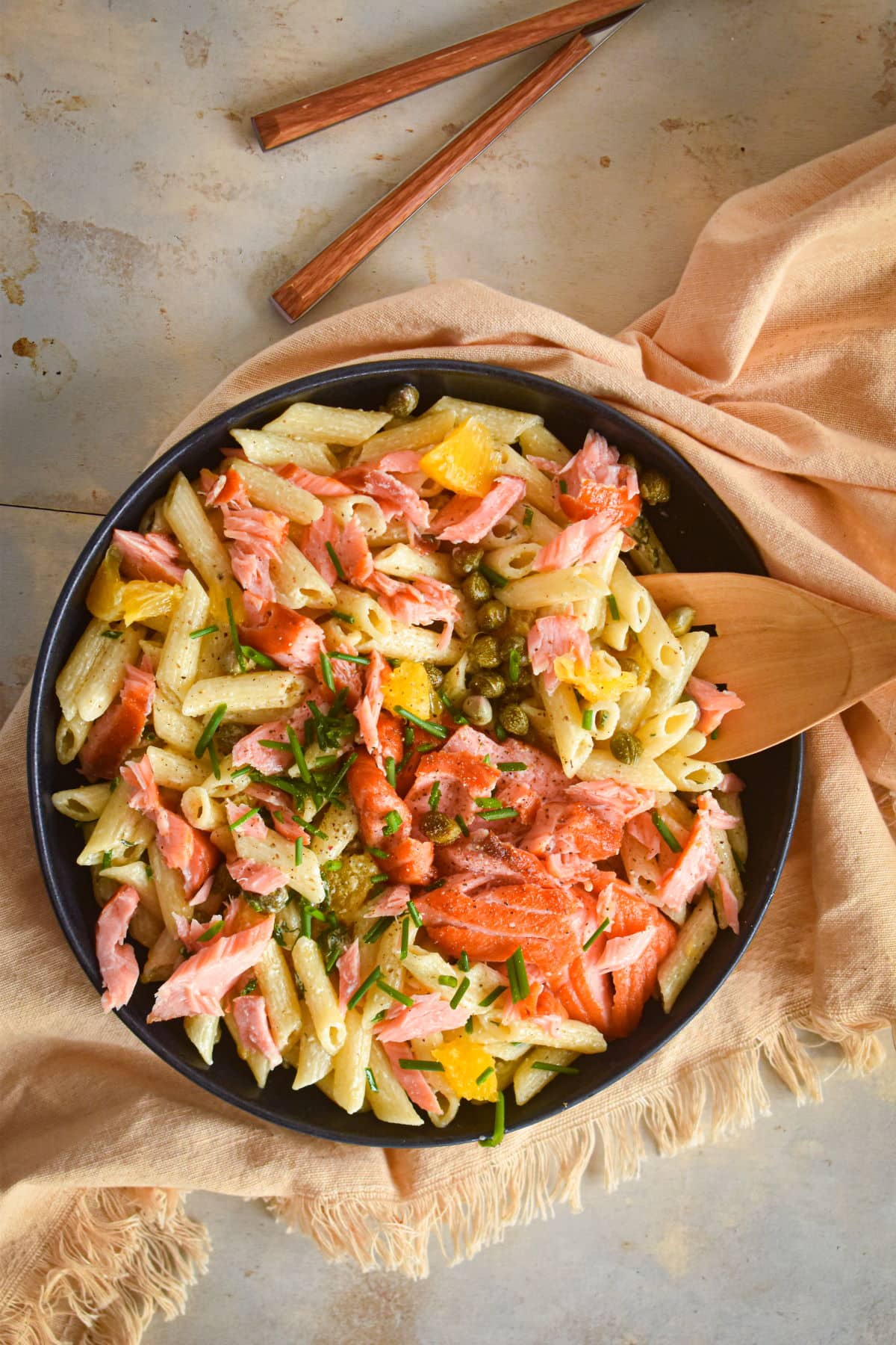 Smoked salmon pasta salad with mandarin oranges and capers in black dish.