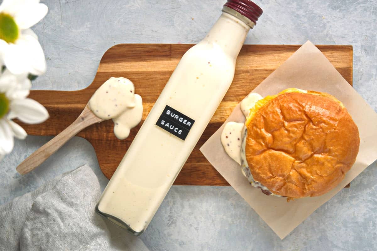 Burger sauce in a bottle on cutting board with hamburger and spoon.