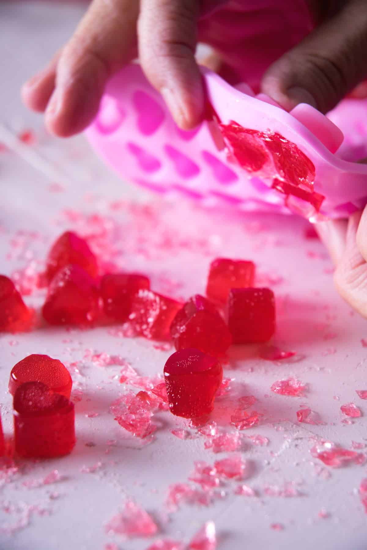 Strawberry heart candies falling out of a pink heart mold.