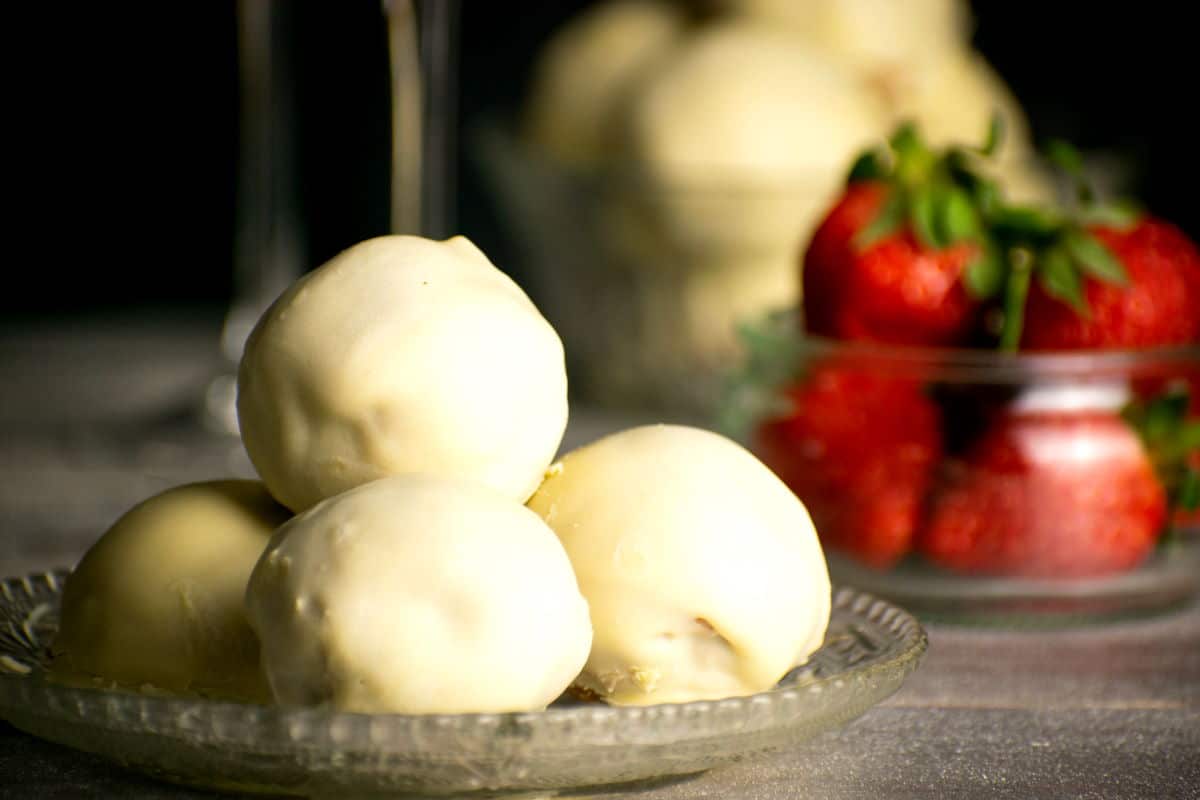 Strawberry champagne cake balls on clear glass dish with strawberries in the background.