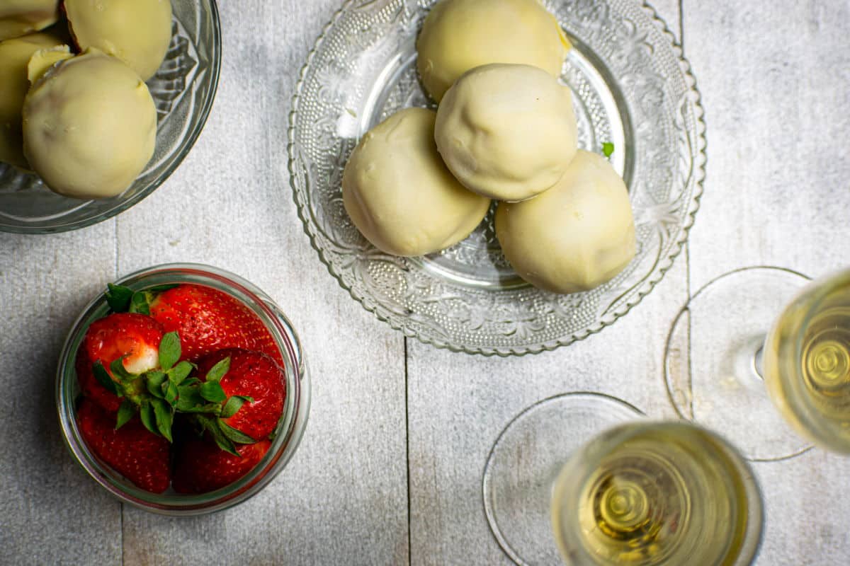 Strawberry champagne cake balls on clear glass dish with champagne glasses and fresh strawberries on the side.