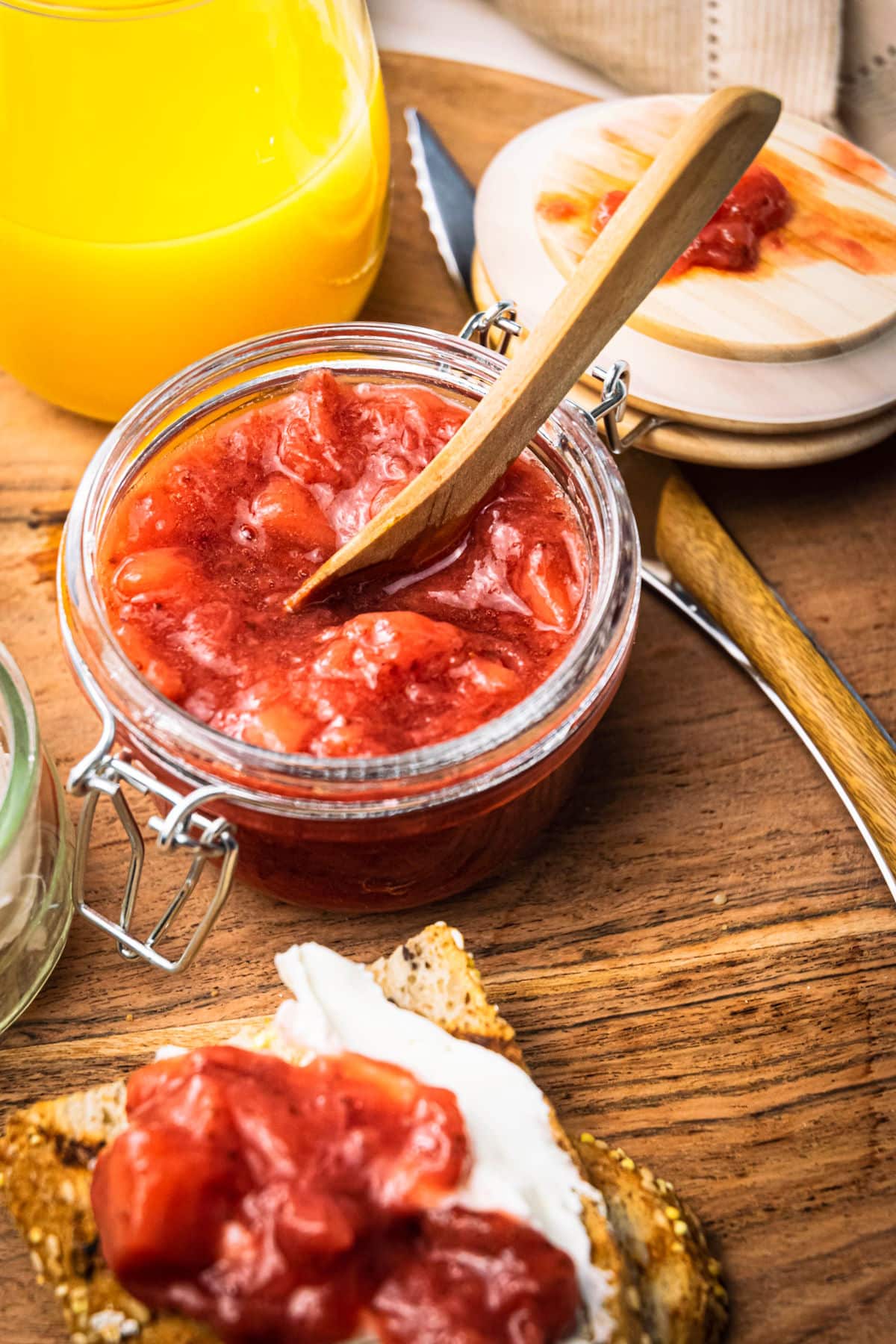 Strawberry compote in a jar and on a piece of toast, orange juice in a glass on the side, wooden background.