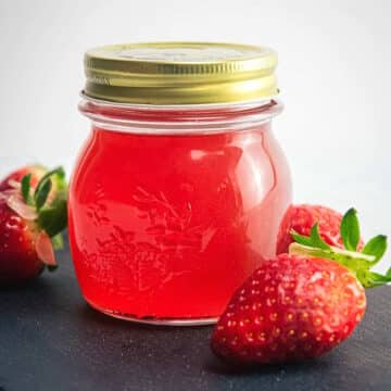 Strawberry liqueur in jar with fresh strawberries on the side.