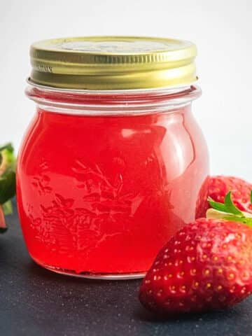 Strawberry liqueur in jar with fresh strawberries on the side.