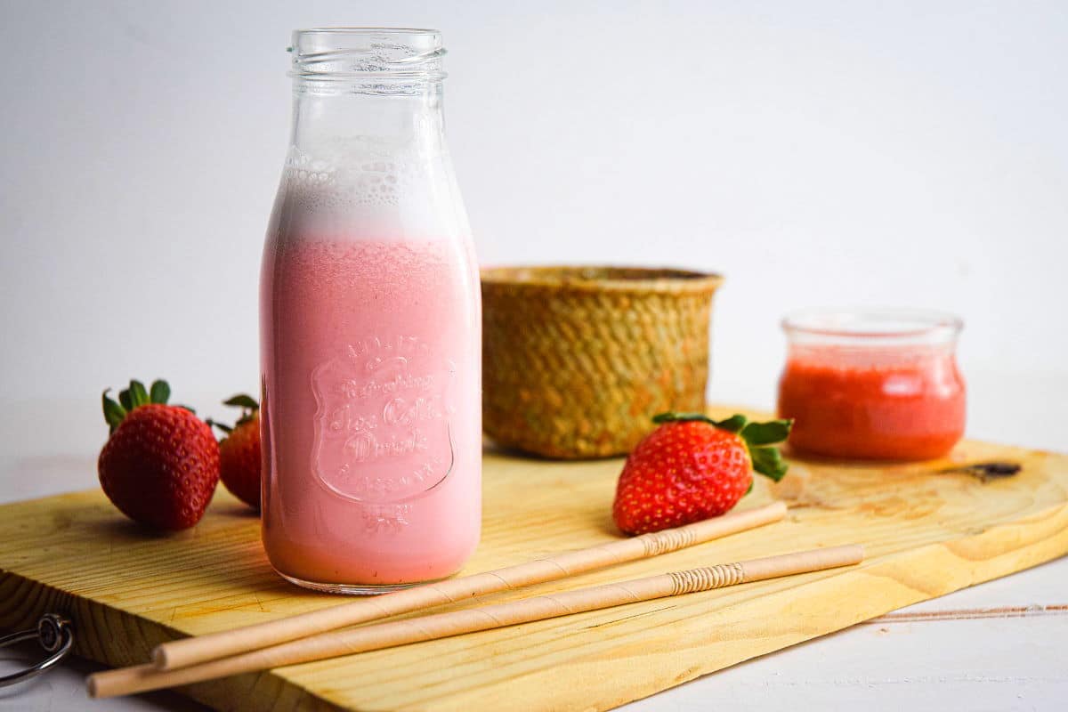 Strawberry Milk in a glass jar and 2 straws on a wooden board.