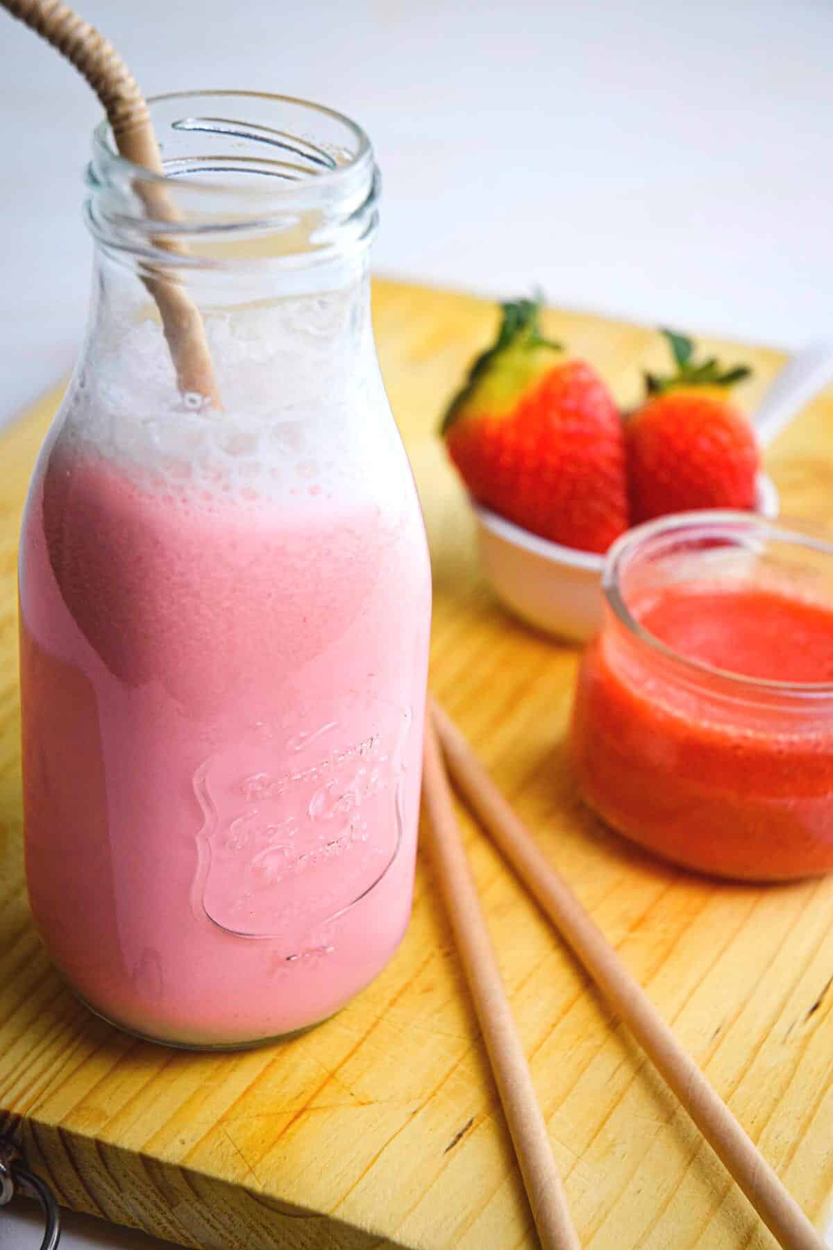 Strawberry Milk in a glass jar with a straw on a wooden board.