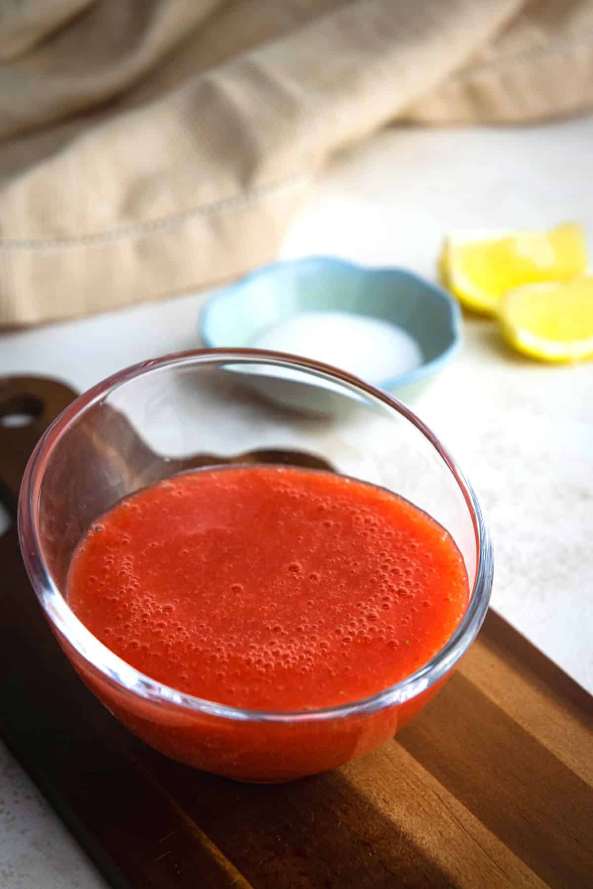 Strawberry puree in a glass bowl on wooden serving board.