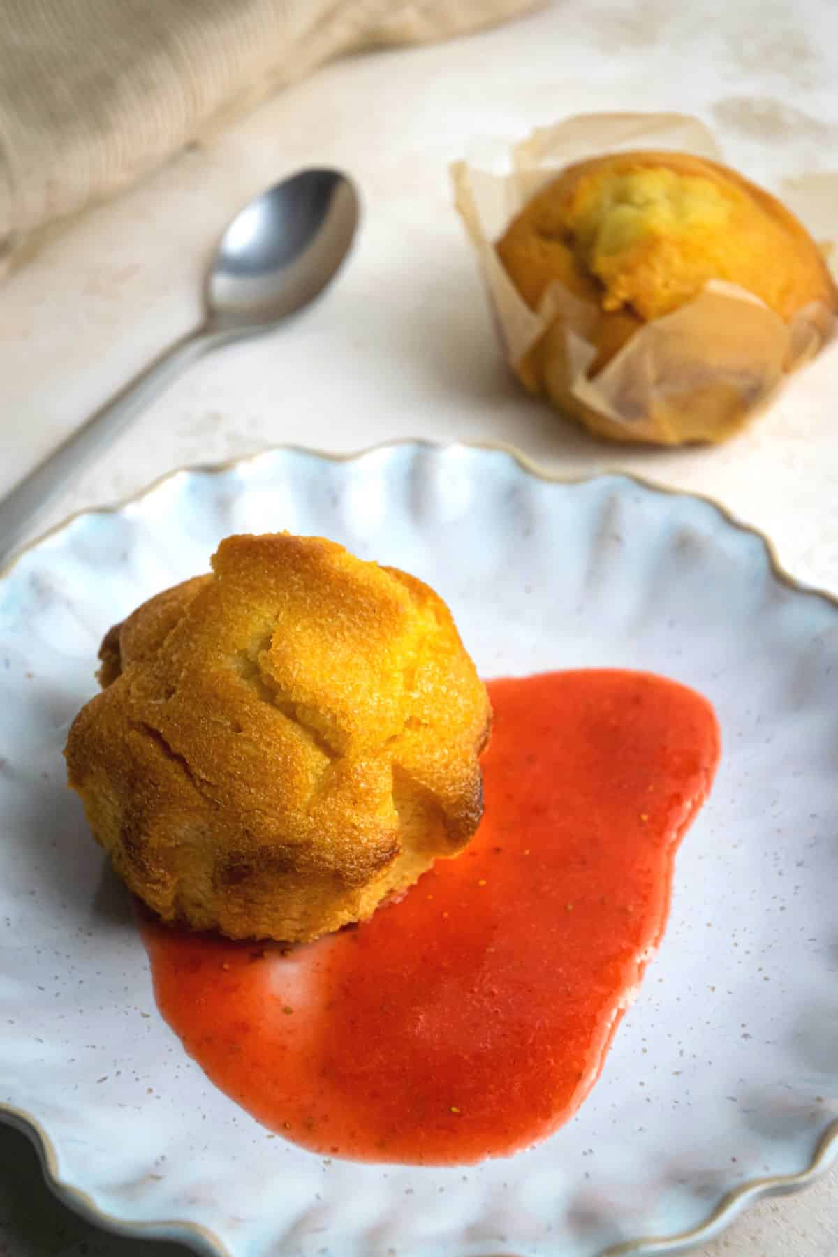 A muffin with strawberry purée on small plate.