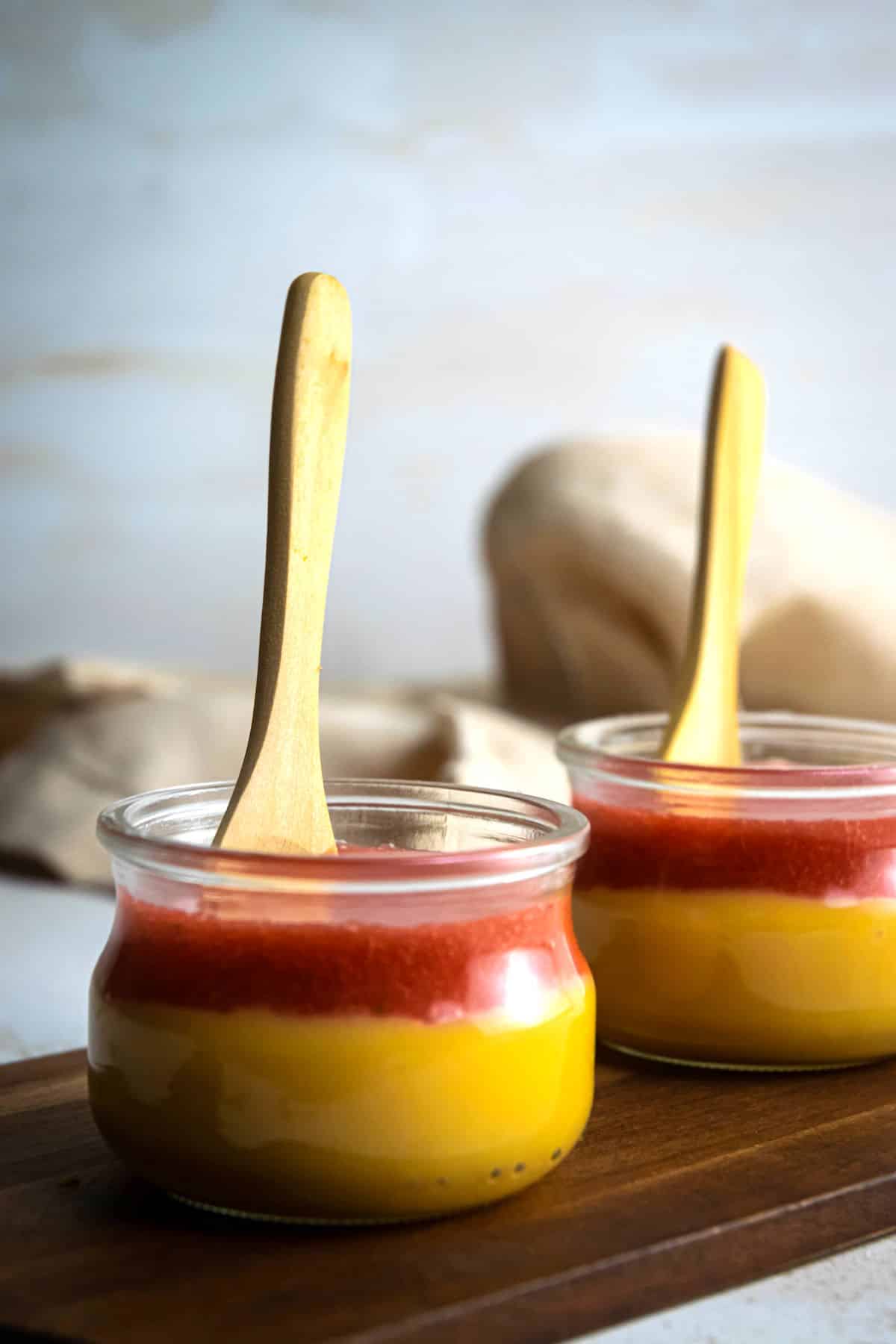 Strawberry puree on top of custard in jars with wooden spoons.