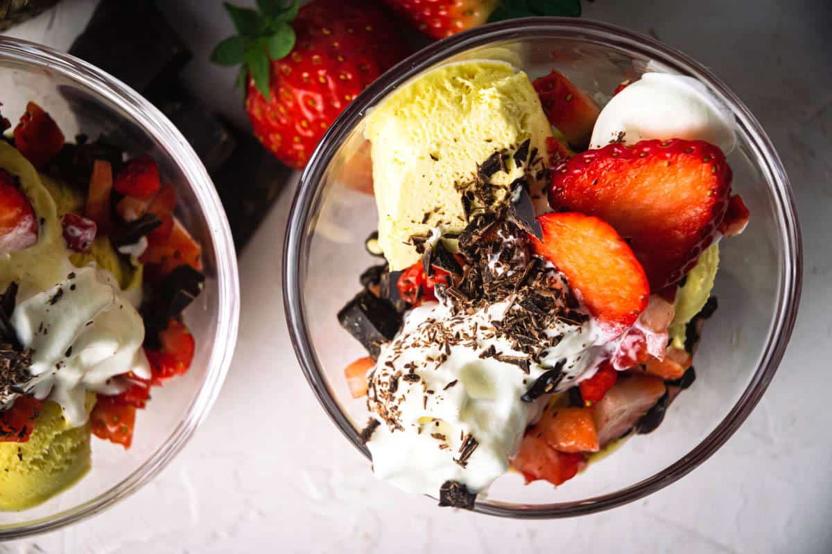 2 strawberry sundaes in dessert bowls with shaved chocolate and strawberries.