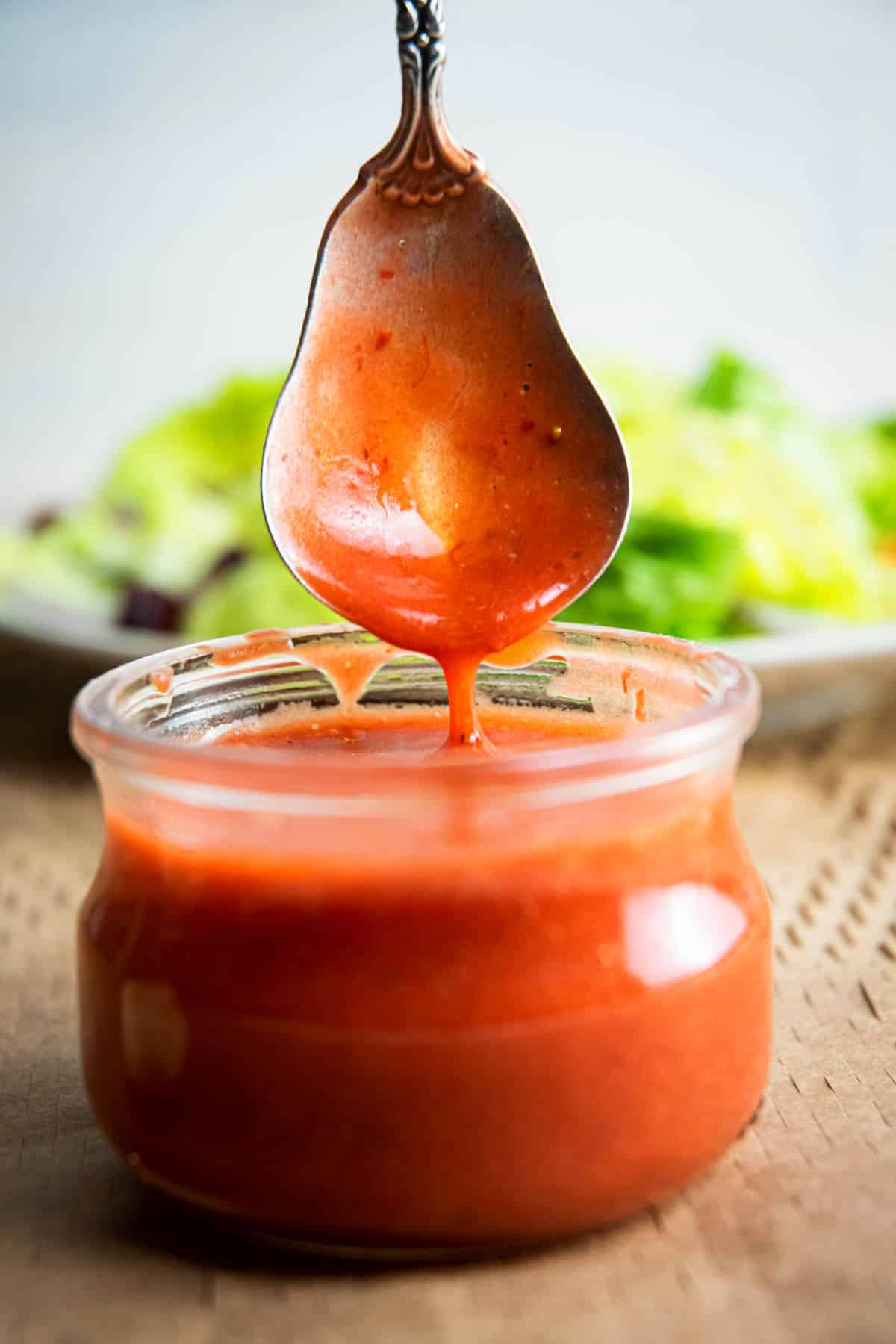 Strawberry vinaigrette drizzling from spoon into jar.
