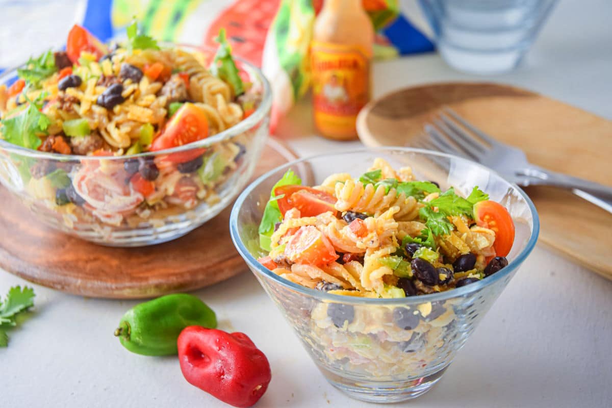 Taco pasta salad in clear bowls. Peppers and forks on the side.