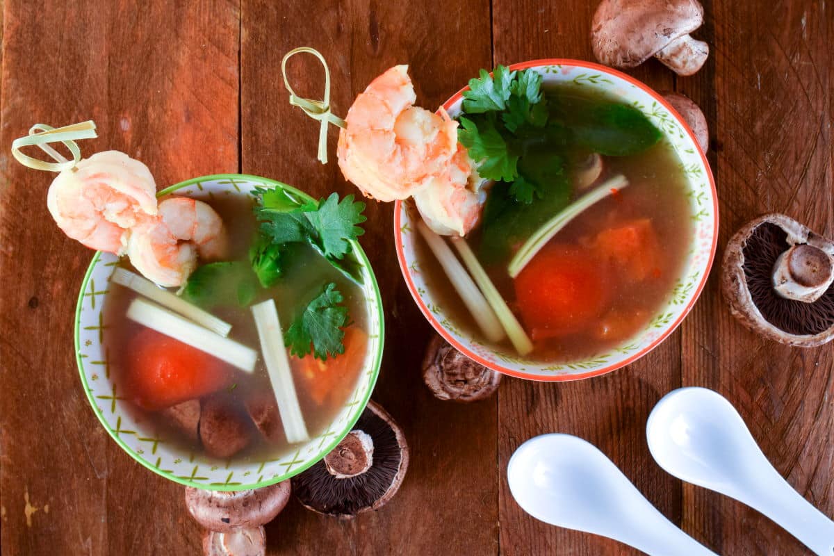 Tom Yum Soup in porcelain bowls with mushrooms and soup spoons on the side.