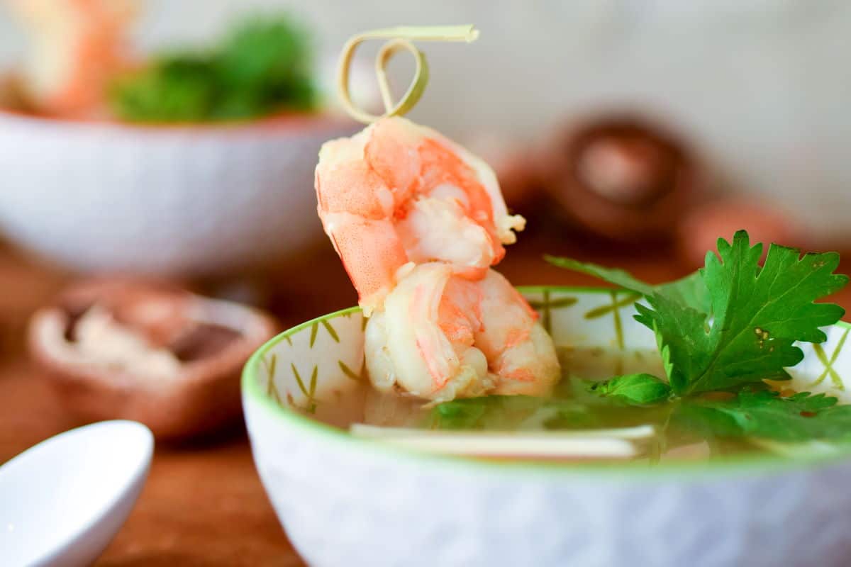 Tom Yum Soup in a porcelain bowl with skewered shrimp.