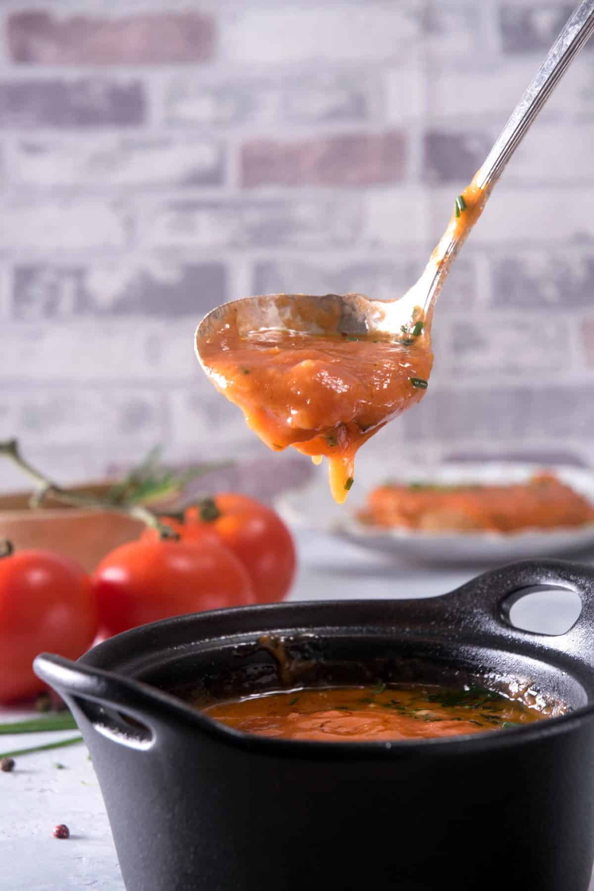 Tomato gravy in a small cast iron bowl, dripping off of a soup spoon.