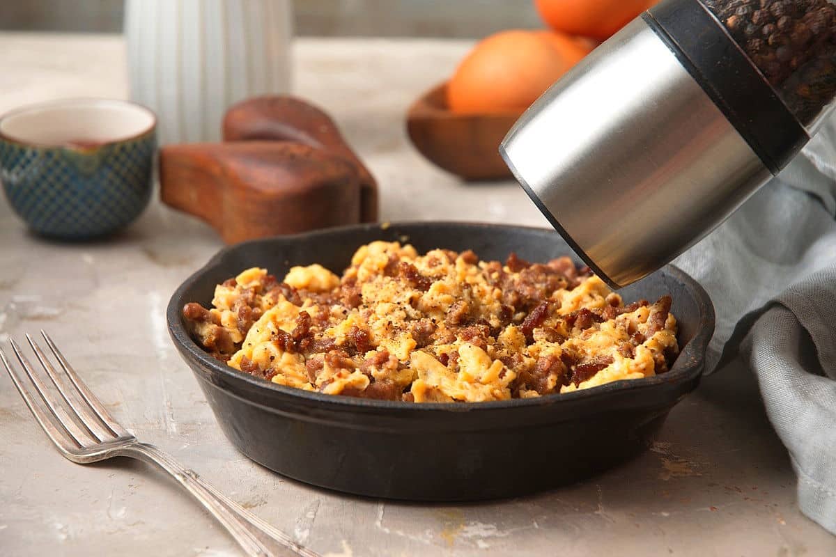 Hamburger scrambled eggs in a cast iron pan with pepper grinder.