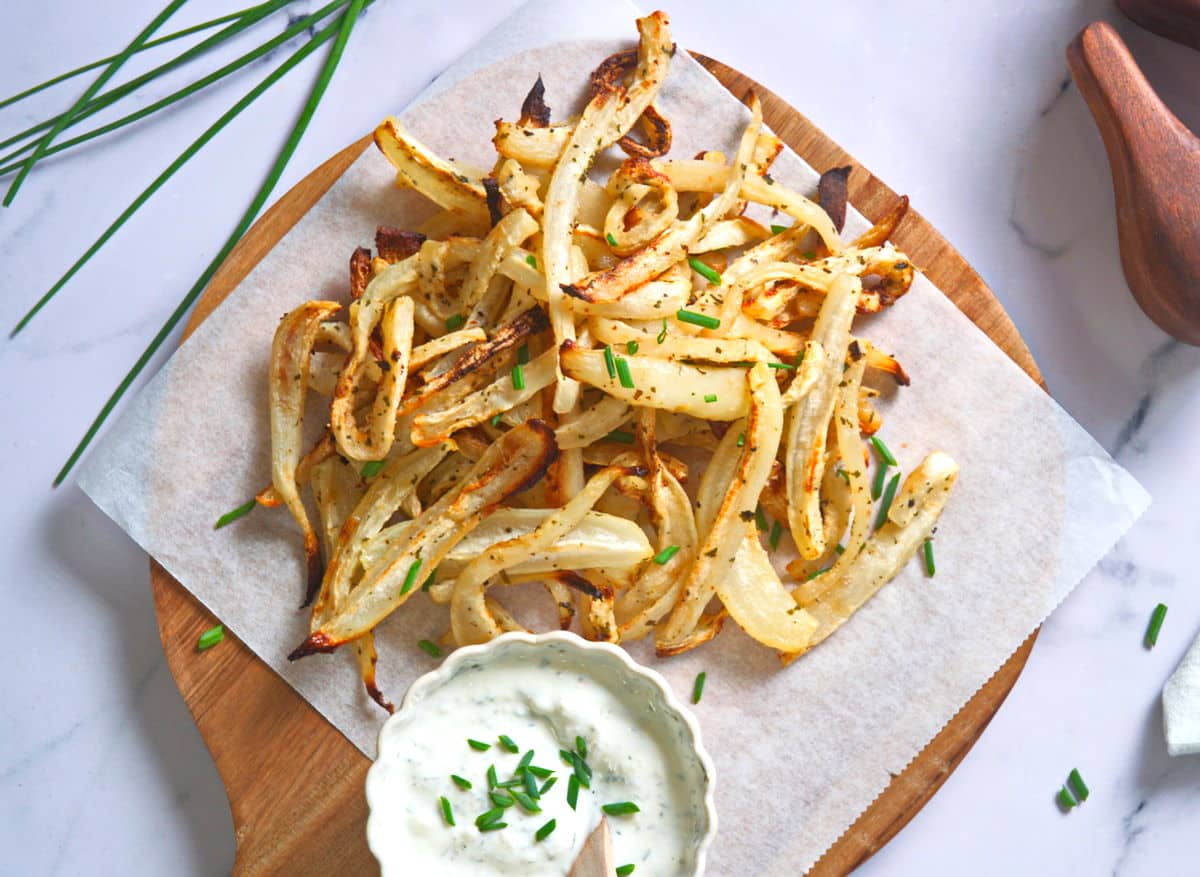 Turnip fries on parchment lined cutting board with yogurt dip in a small bowl.