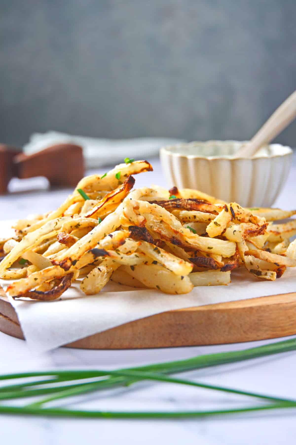 Golden, crispy, baked turnip fries on parchment-lined wooden board.