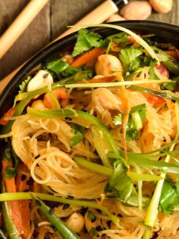 Vegan Pad Thai in a black bowl with chopsticks and peanuts on the side.