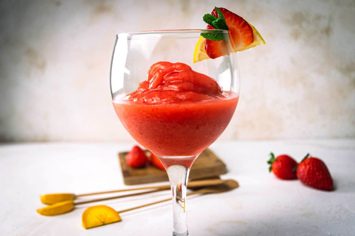 Virgin frozen strawberry daiquiri in a glass with a strawberry, mint and lemon garnish.