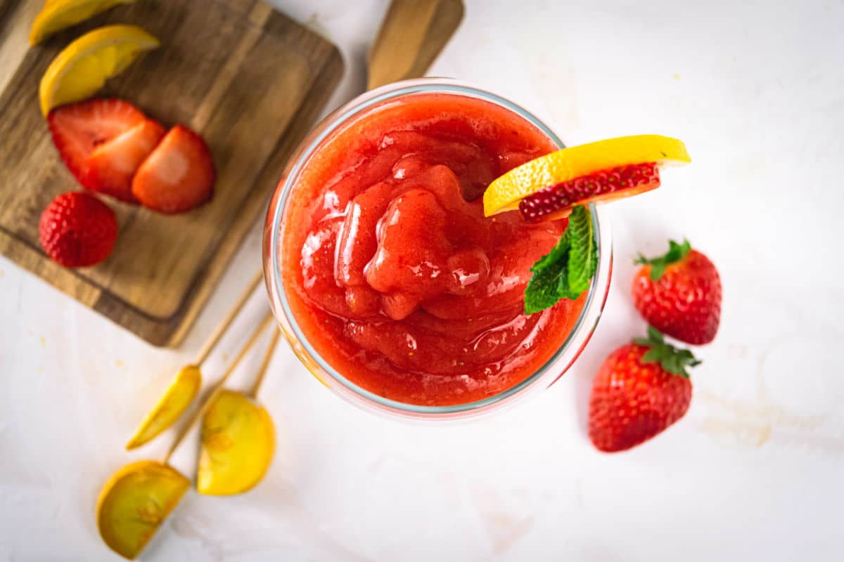 Virgin frozen strawberry daiquiri in a wine glass and fresh strawberries on the side.