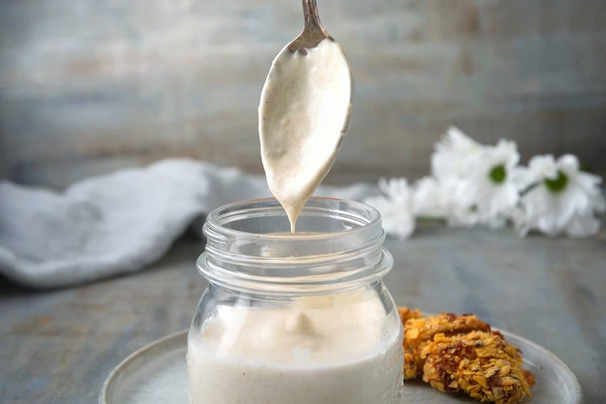 White BBQ sauce in a small jar with a spoon.