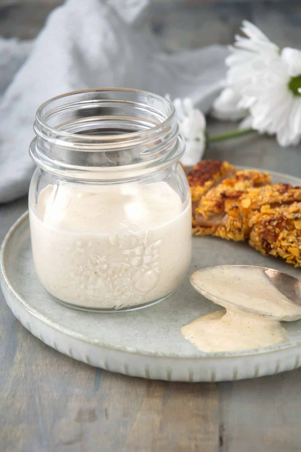 White BBQ sauce in a small jar on a plate.