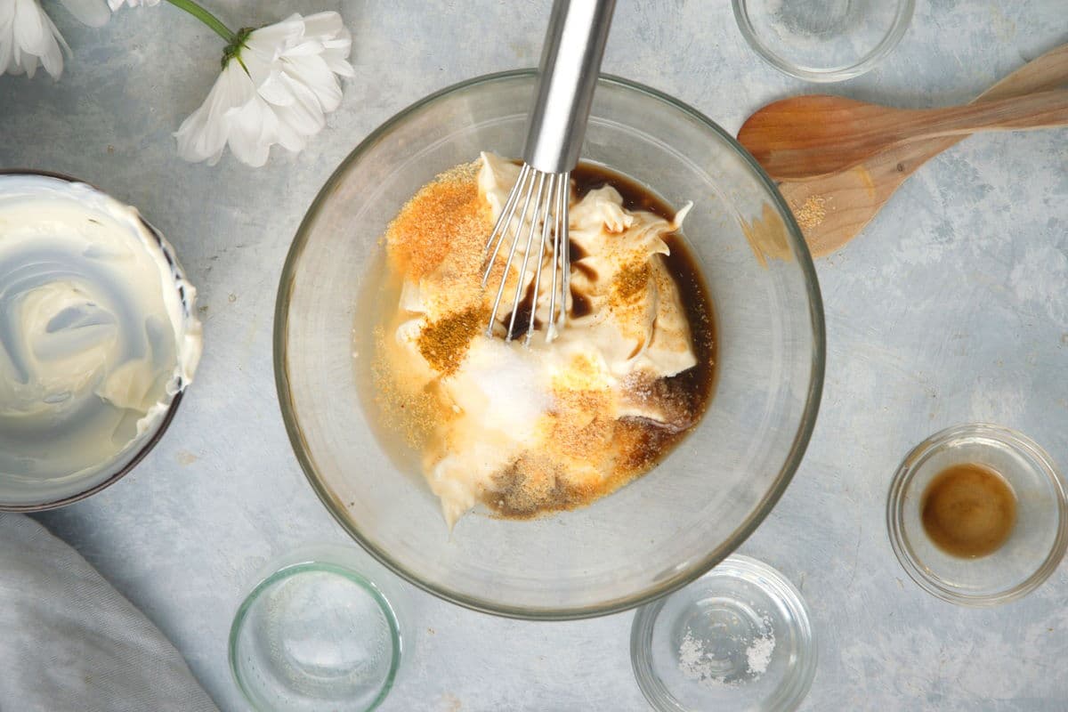 Mayo and spices in a small glass bowl with a whisk.
