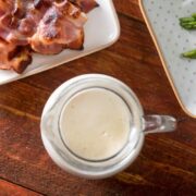 White gravy in a jar with bacon and asparagus on the side--top view.