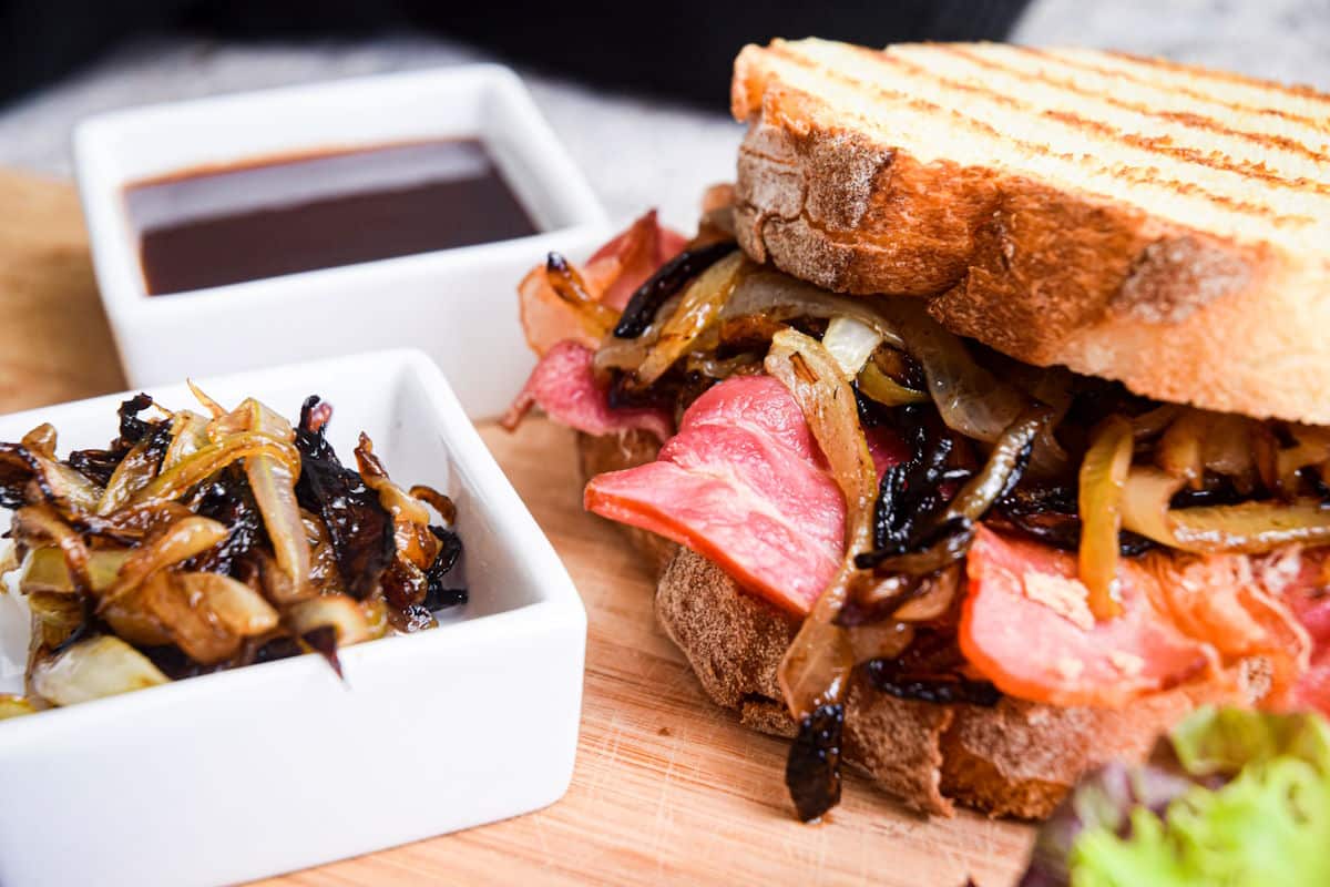 Bacon sandwich on board with caramelized onions and sauce.