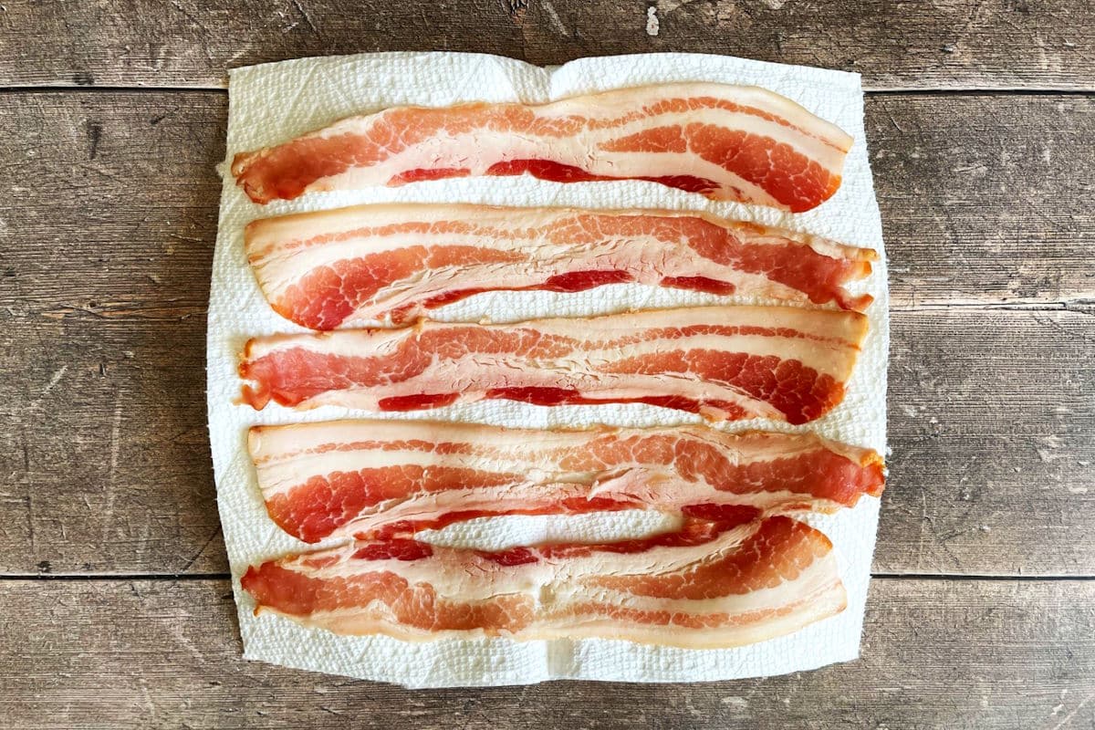 Raw bacon strips on paper towel-lined plate.