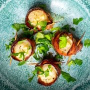 Bacon wrapped scallops with parsley on blue plate.