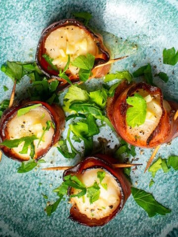 Bacon wrapped scallops with parsley on blue plate.