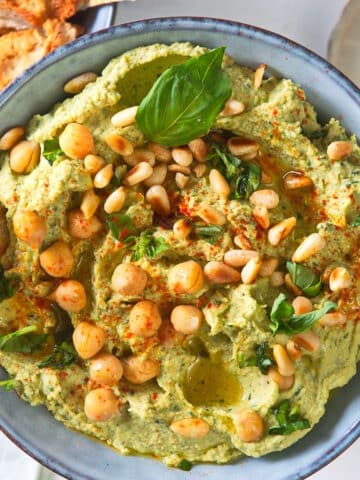 Fresh basil hummus in bowl with pine nuts.