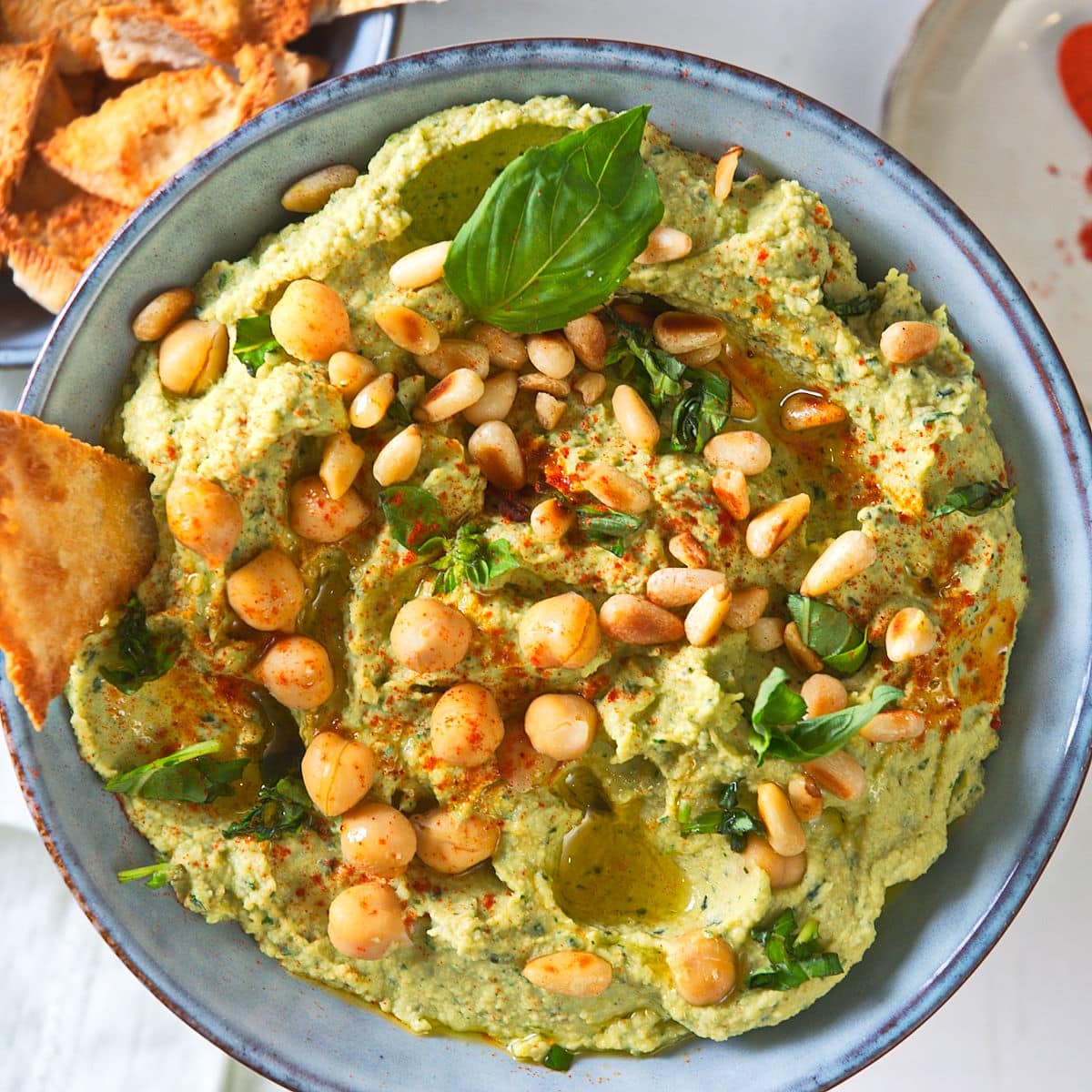 Fresh basil hummus in bowl with pine nuts.