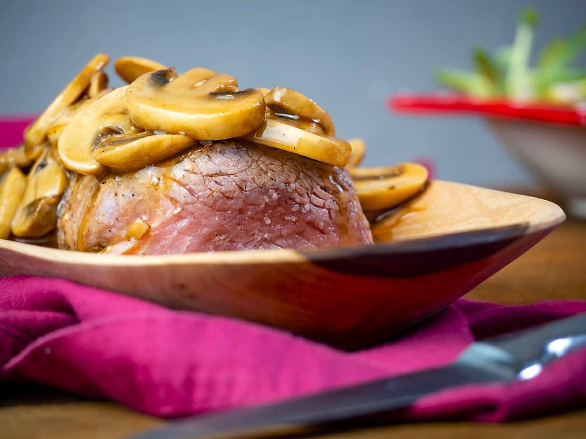 Beef tenderloin covered in mushroom sauce in serving dish.