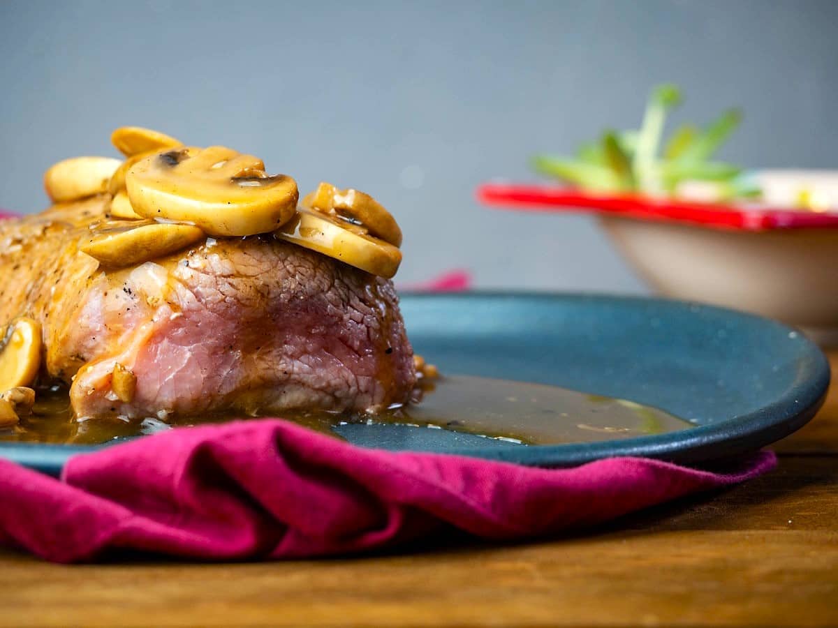 Beef tenderloin covered in mushroom sauce on plate.