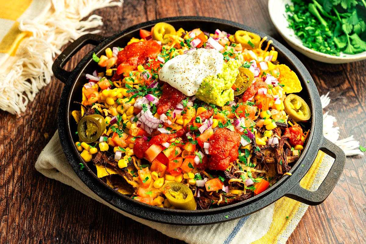 Bison brisket nachos in cast iron pan with toppings.