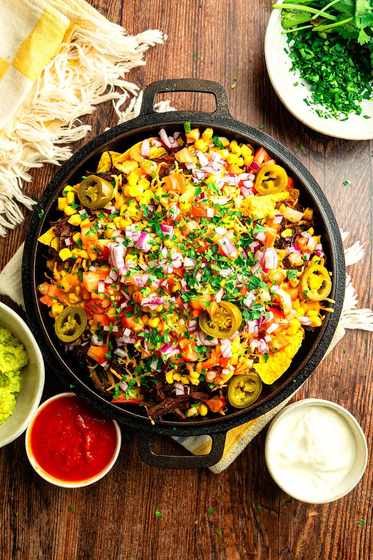 Bison brisket nachos in cast iron pan with toppings and dips on the side.