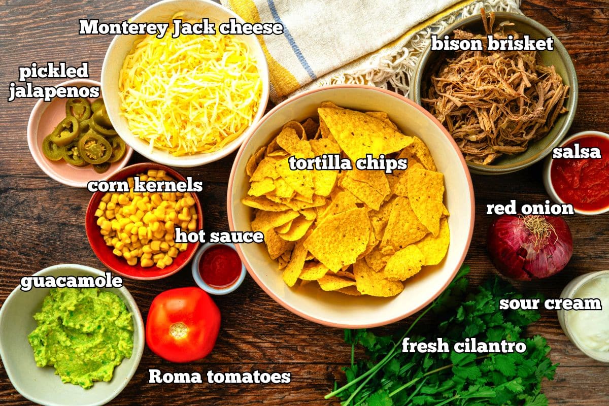 Bison brisket nachos ingredients labeled on wooden background.