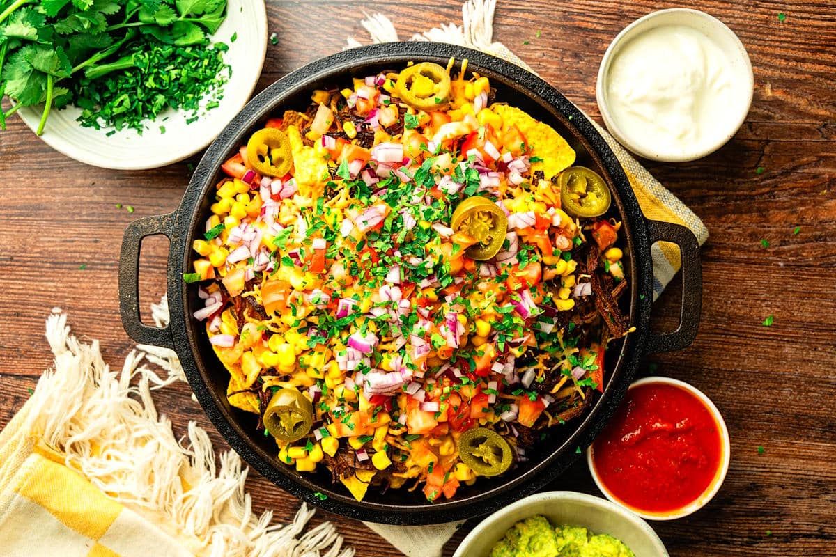 Bison brisket nachos with fresh toppings assembled in cast iron pan.