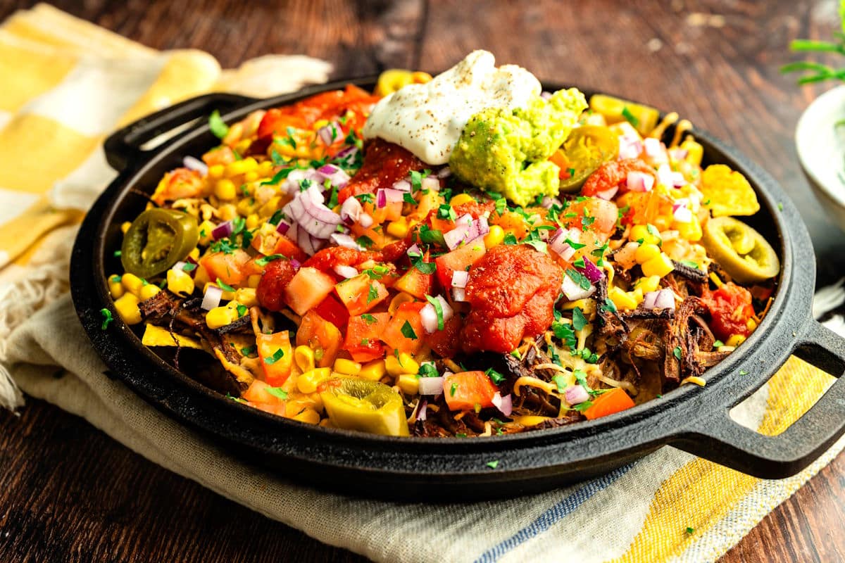 Bison brisket nachos with fresh toppings and condiments, assembled in cast iron pan.