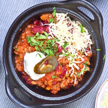 Bison chili with toppings in cast iron dish.