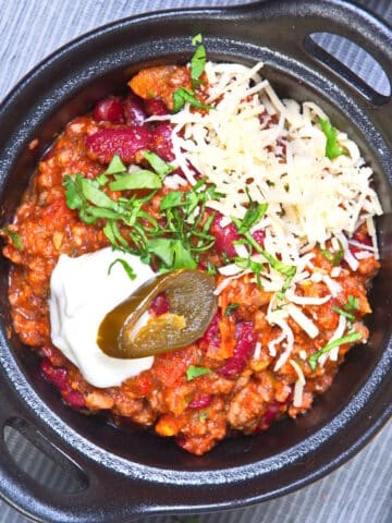 Bison chili with toppings in cast iron dish.