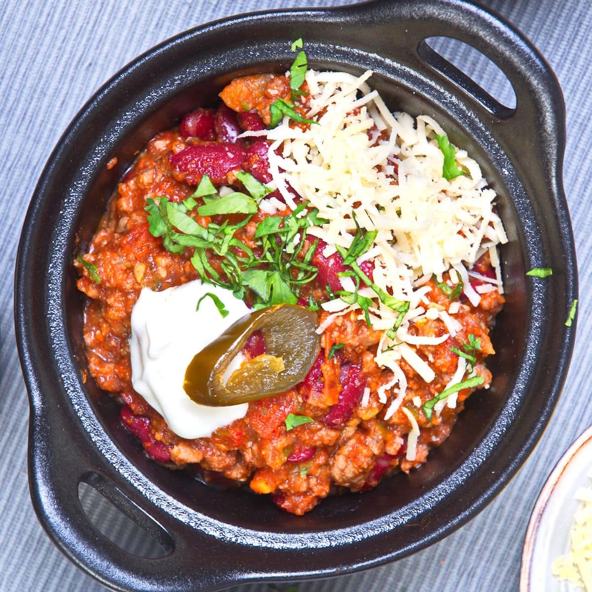 Bison chili with toppings in cast iron dish.