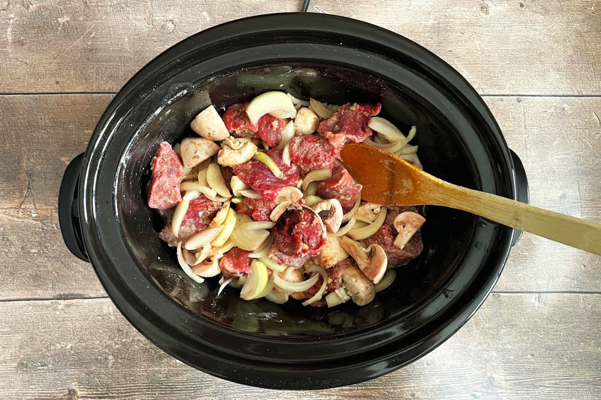 Bison stew ingredients in slow cooker with wooden spoon.