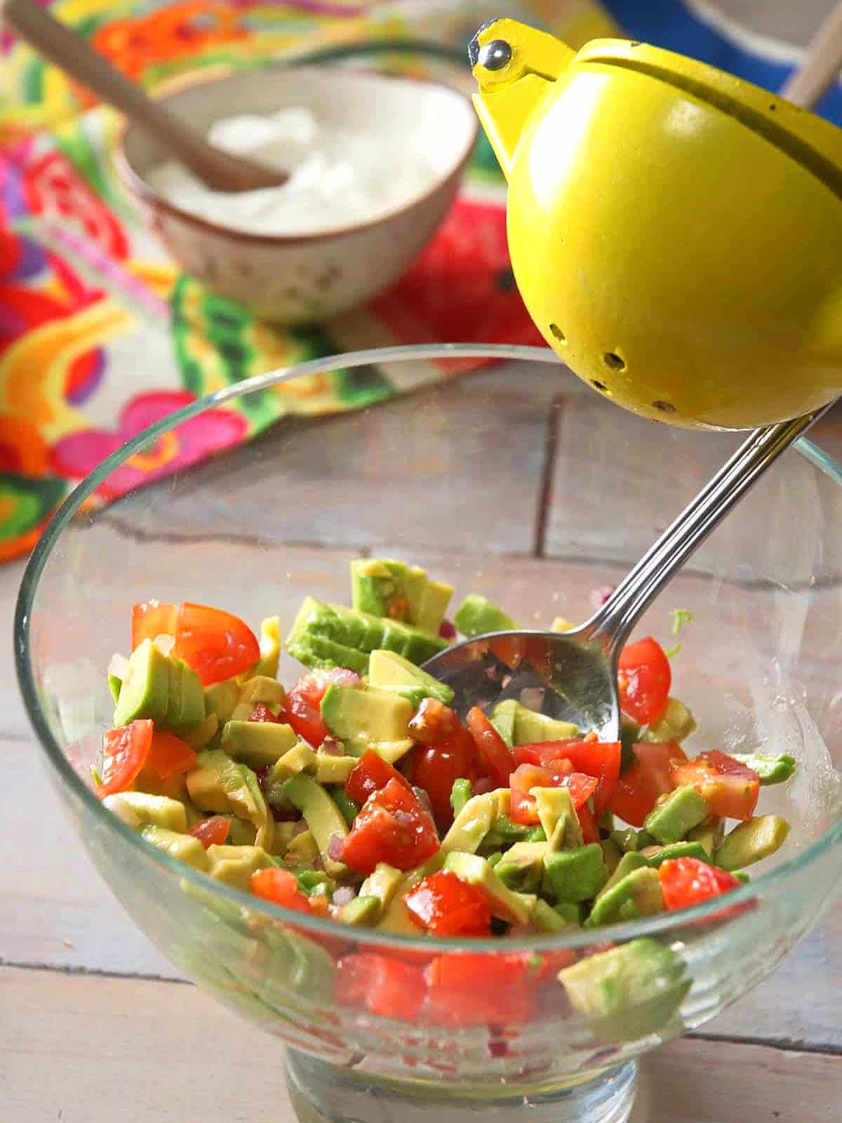 Chopped avocado and tomatoes in bowl with lemon squeezer.