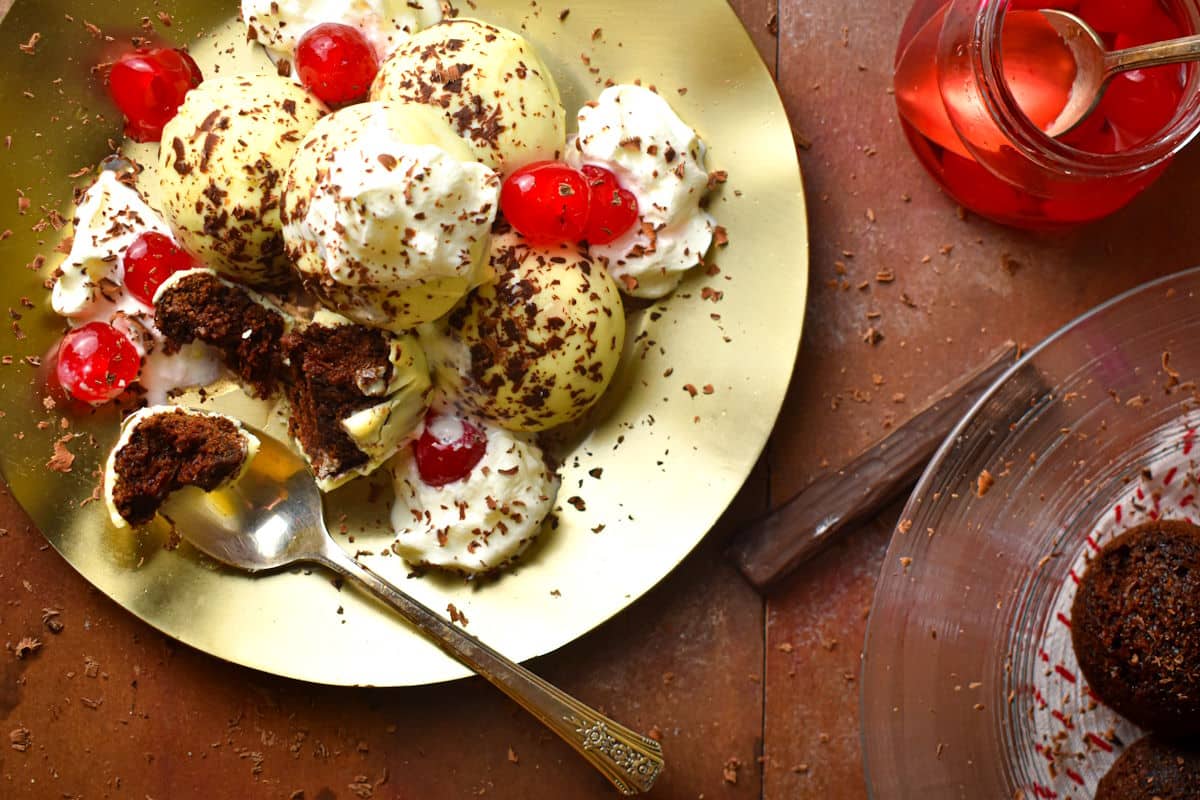 Black Forest cake balls stacked on plate, one cut open with spoon.