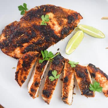 Blackened chicken breast on plate with lime wedges and cilantro.