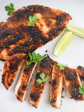 Blackened chicken breast on plate with lime wedges and cilantro.